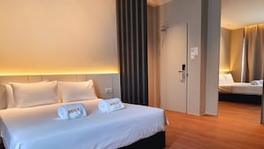 A hotel room with a large bed, two towels with the name "ROXY" on them, a wooden floor, and a door leading to another room. - ROXY HOTEL MALIHAH (Kuching)