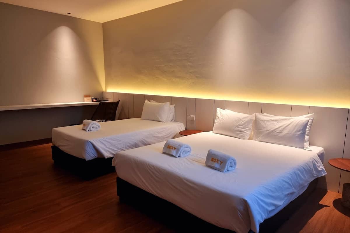 Hotellihuoneessa on kaksi sänkyä, joissa on valkoiset lakanat ja pyyhkeet, joissa lukee nimi ”ROXY”. Huoneessa on puulattia ja moderni sisustus, johon kuuluu vaaleanvärinen seinä ja kattovalaisin.