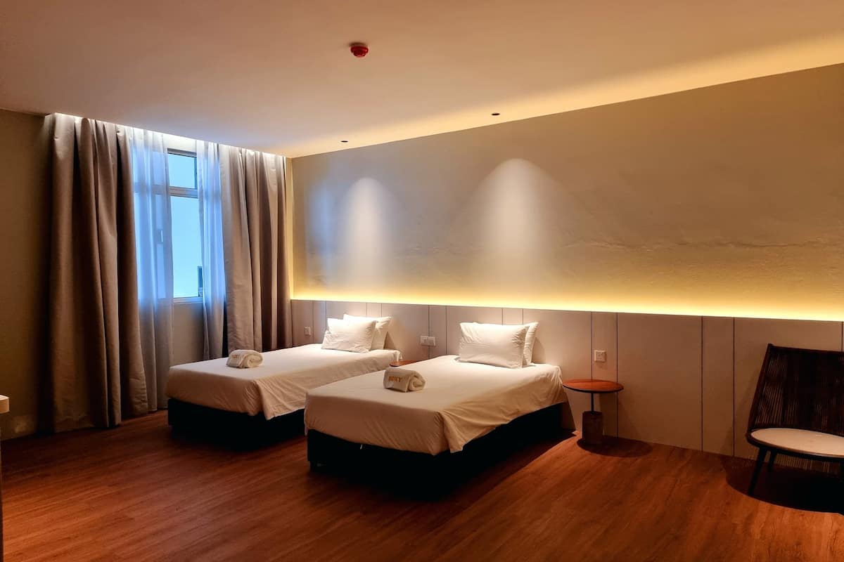 Hotellihuone, jossa on kaksi sänkyä, puulattia, pieni pöytä ja tuoli.