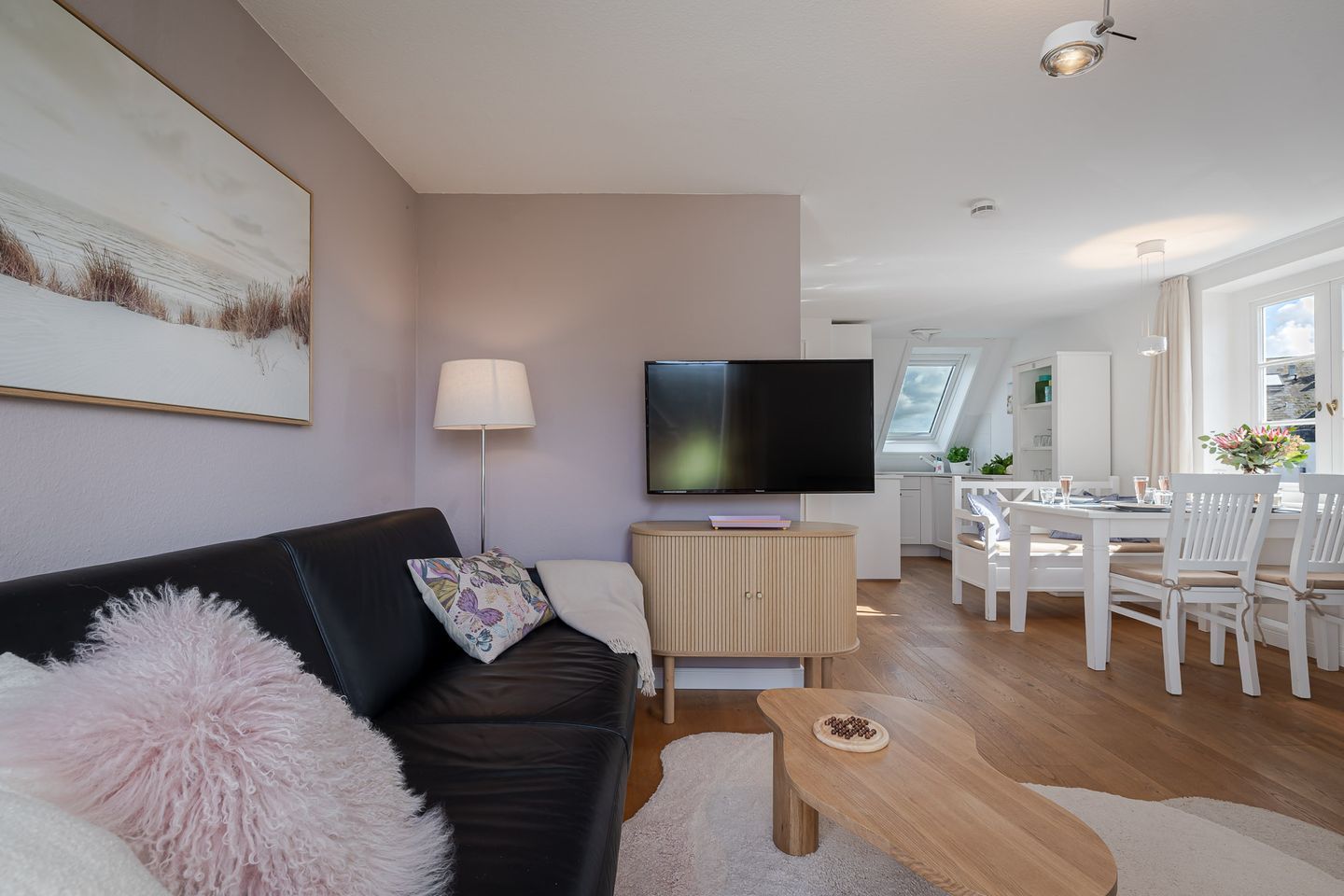 A modern living room with a flat-screen TV, a sofa, a coffee table, and a dining area with chairs.