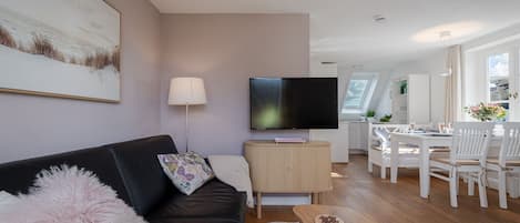 Uma sala de estar moderna com televisão de tela plana, sofá, mesa de centro e área de jantar com cadeiras.