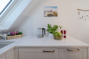 Eine moderne Küche mit Oberlicht, einem Blumentopf, einer Kaffeemaschine und einer Wanddekoration mit Fischmotiven.