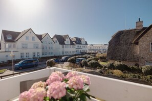 Eine Wohnstraße mit Häusern, parkenden Autos und einem Balkon mit Blumen.