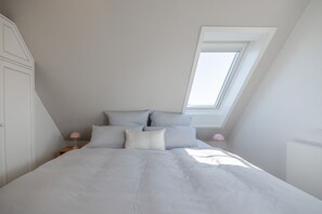 Un dormitorio con tragaluces, una cama con muchas almohadas y lámparas de noche.