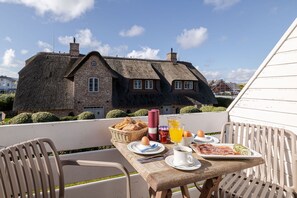 A table set with breakfast items on a balcony with a thatched-roof building in the background.