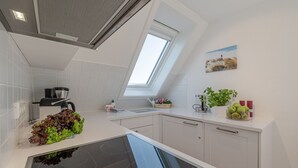 A modern kitchen with a skylight, white cabinets, a black stove, and a countertop with a plant and apples. - Nordseezauber - North Sea magic - Holiday apartment near the beach with sea view in (Wenningstedt-Braderup (Sylt))