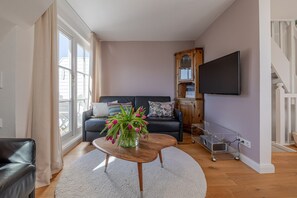 Una sala de estar con un sofá, una mesa de centro con flores, un televisor y una escalera.