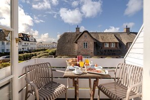 A balcony with a table set for breakfast, overlooking a traditional building with a thatched roof.