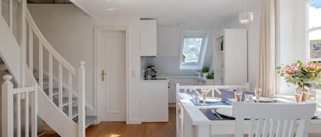 Une cuisine moderne avec des meubles blancs, un coin repas avec une table dressée pour deux personnes, et un escalier avec des rampes blanches.