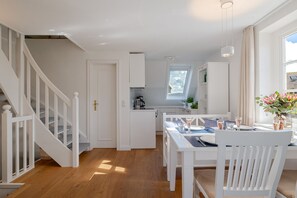 A modern kitchen with white cabinetry, a dining area with a table set for two, and a staircase with white railings.