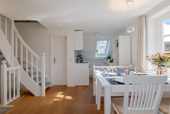 A modern kitchen with white cabinetry, a dining area with a table set for two, and a staircase with white railings.