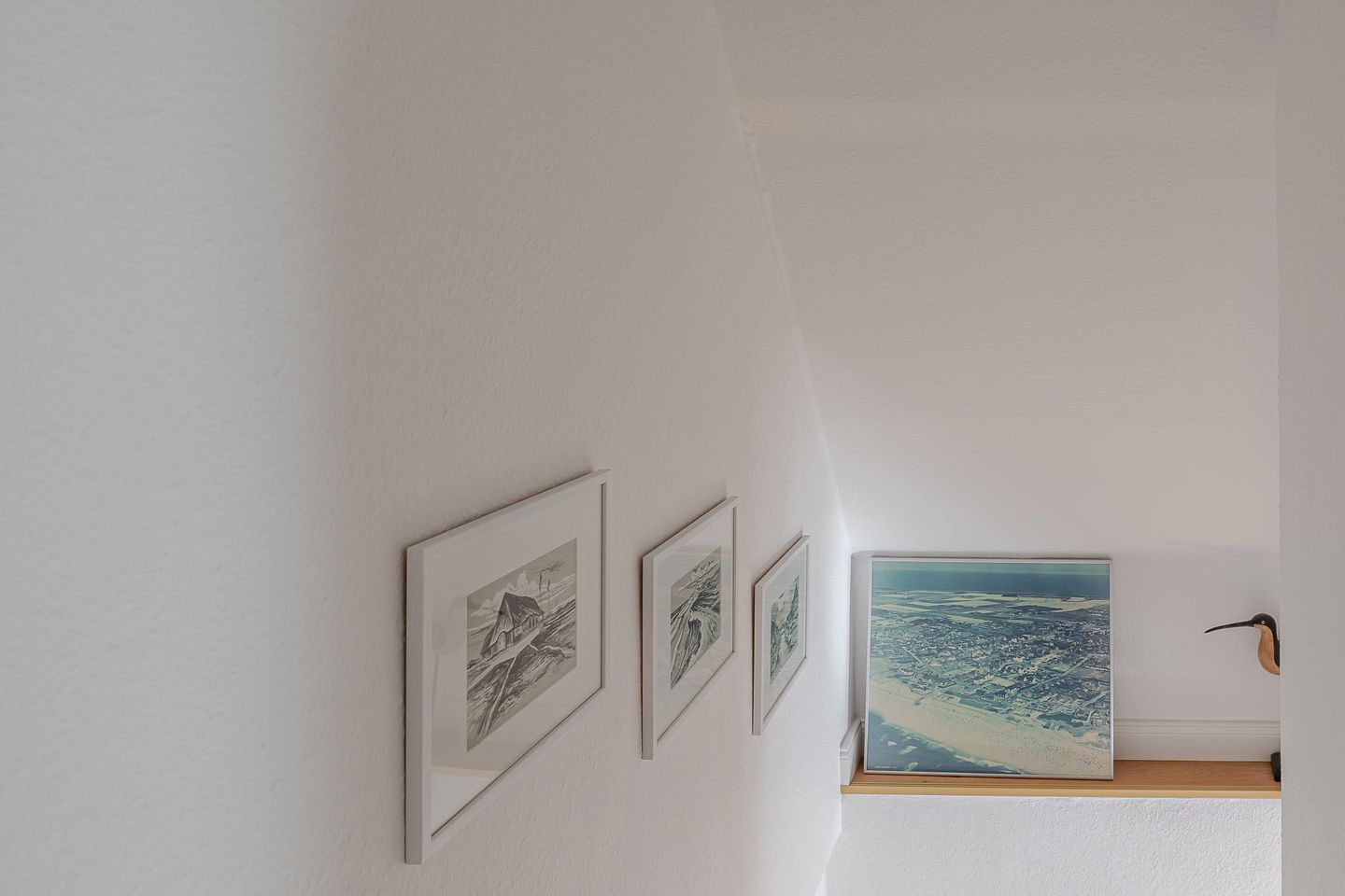 Una habitación con una pared blanca que muestra tres obras de arte enmarcadas y un cuadro grande en un estante de madera.