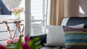 A modern living room with a black leather sofa, a white cushion, and a colorful woven pillow. A small wooden table with a vase of pink flowers is visible in the background. - Nordseezauber - North Sea magic - Holiday apartment near the beach with sea view in (Wenningstedt-Braderup (Sylt))