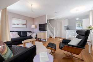 A modern living room with a black sofa, a wooden coffee table, a black leather chair, and a television.