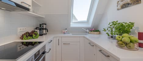 A compact kitchen with white cabinetry, a built-in oven, a coffee maker, and a window above the sink.