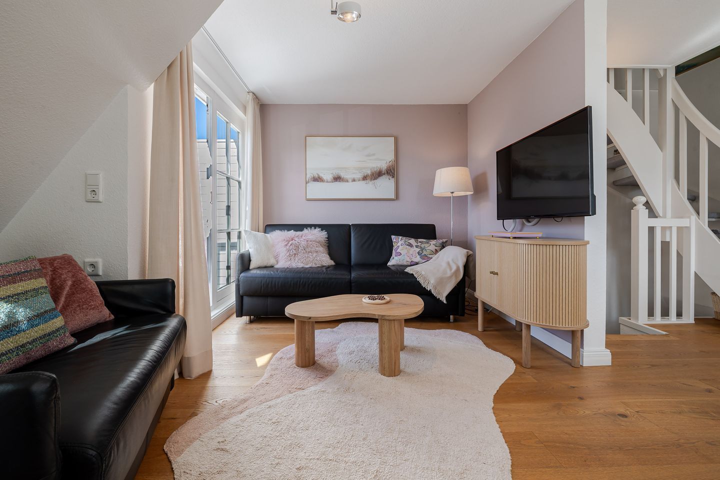 Un salon avec un canapé en cuir noir, une table basse en bois et un téléviseur posé sur un meuble en bois.