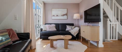 Una sala de estar con un sofá de cuero negro, una mesa de centro de madera y un televisor sobre un mueble de madera.