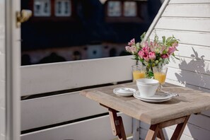 A wooden table with a white cup, a glass of orange juice, and a vase of pink flowers on a balcony.