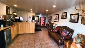A lobby with a wooden reception desk, a leather sofa, framed pictures on the wall, and a mounted deer head. - New Western Inn & Suites (Fillmore)