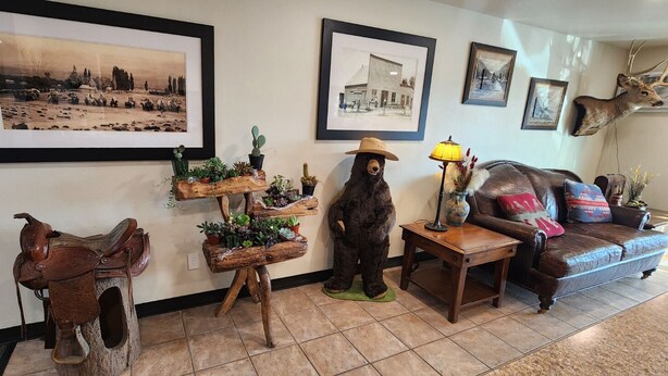 A room with a leather sofa, a mounted deer head, framed historical photos, a cactus planter, and a bear statue. - New Western Inn & Suites (Fillmore)