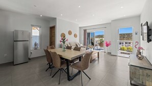 Une cuisine moderne dotée d’un réfrigérateur encastré, un coin repas avec une table et des chaises en bois, et un balcon offrant une vue sur le paysage.
