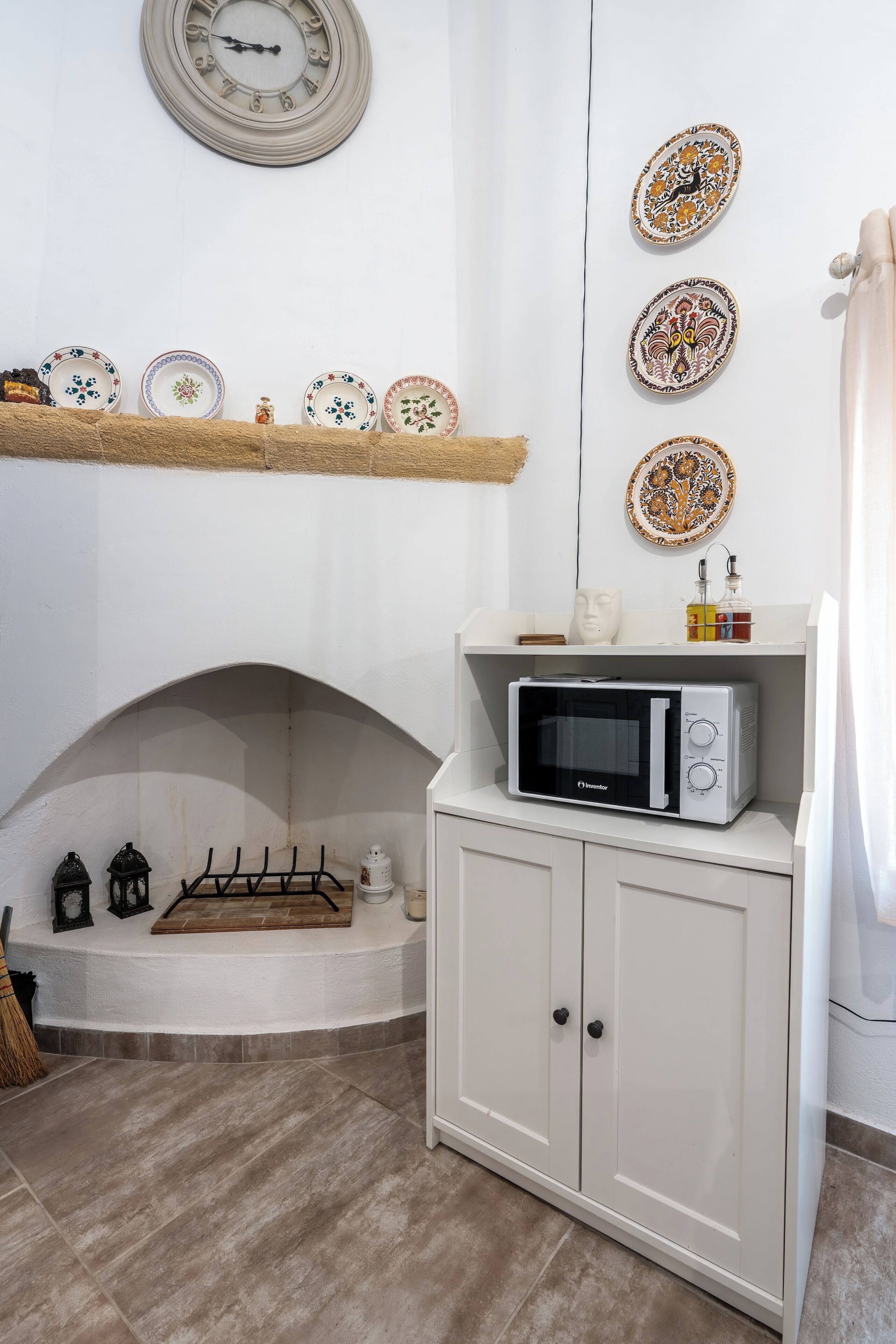Una cocina con microondas sobre un mueble, una repisa con platos decorativos y una chimenea con una escoba.