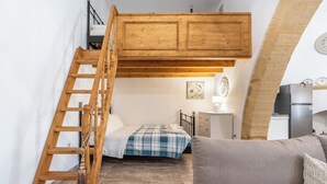 A bedroom with a loft bed, a wooden ladder, a bedside table, a lamp, and a small kitchenette. - Amalia's Traditional Home In Paradisi (Paradeisi)
