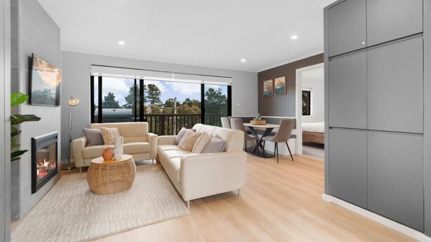 A modern living room with a fireplace, a sofa set, a dining area, and large windows offering a view of the outdoors. -  Cosy townhouse with picturesque lakeside views. (Jindabyne)