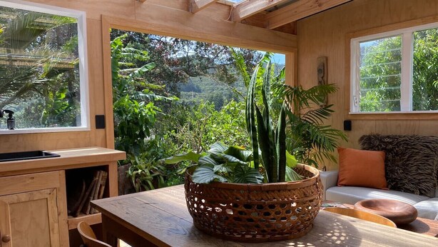 Un interno in legno con un tavolo, sedie, un cesto di piante e vista sul verde circostante.