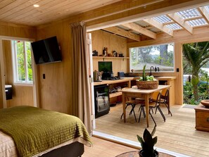 A cozy room with a bed, a TV, and a view of a kitchen and outdoor area.