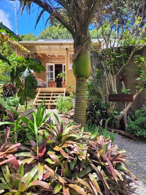 A tropical garden with a wooden deck leading to a house, surrounded by various plants and a sign reading 'The Garden House.'
