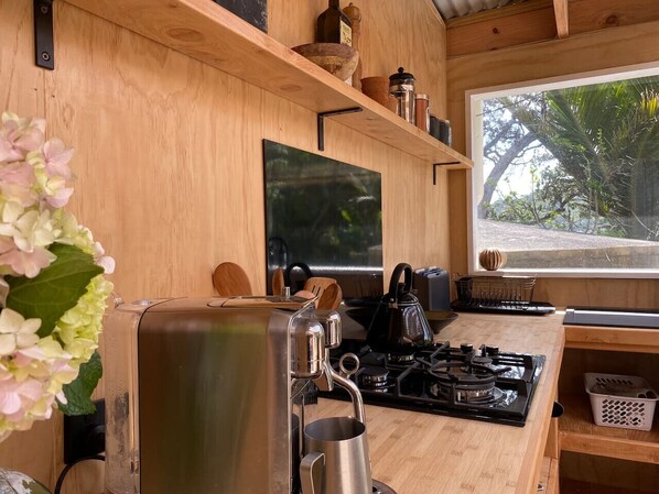 A kitchen with a gas stove, a kettle, and wooden shelves with kitchenware.