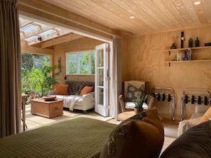 A cozy room with a bed, a sofa, a dining table, and a window overlooking greenery.