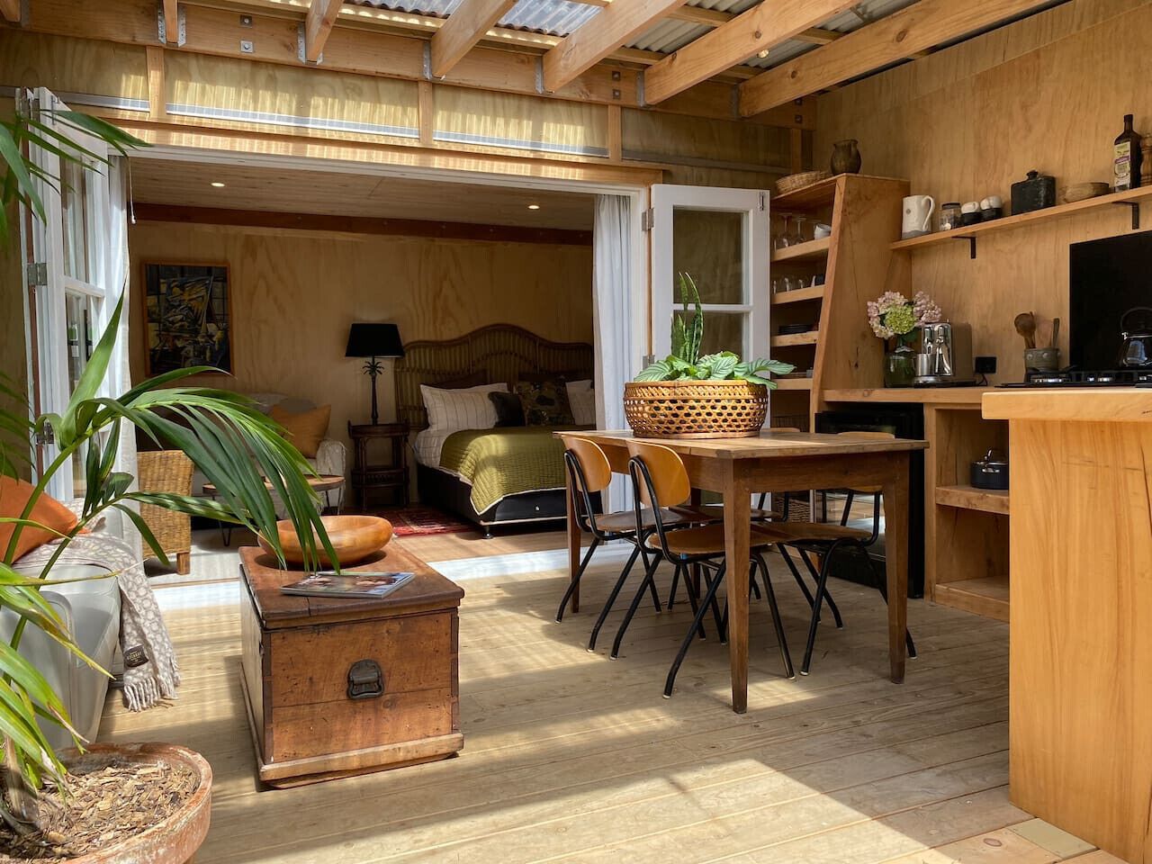 Una habitación acogedora con cama, una mesa de comedor con sillas, un aparador de madera y un ventanal grande.