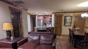 Un salon spacieux avec un canapé en cuir marron, une table basse en bois et un coin repas comprenant une table et des chaises en bois.