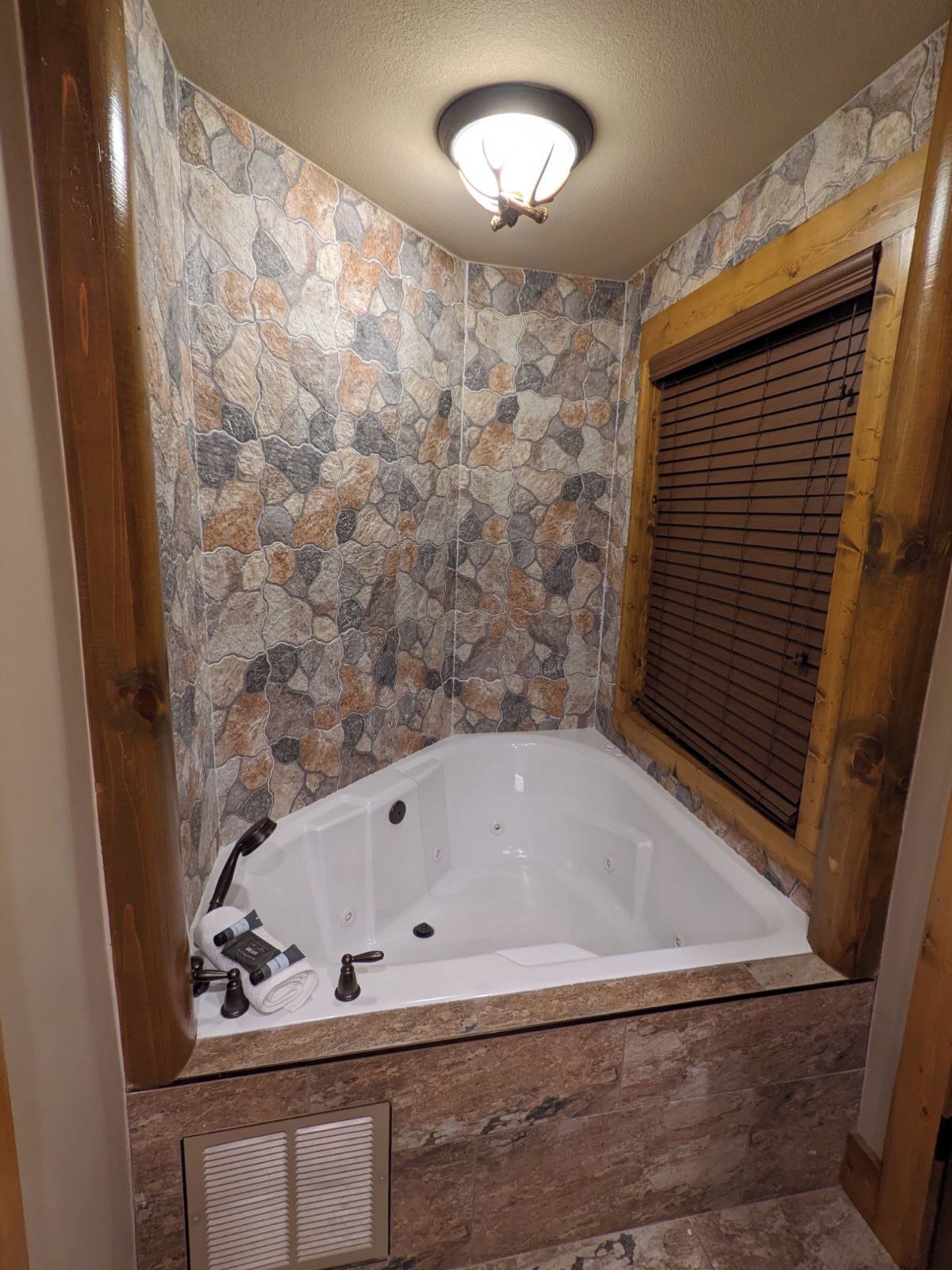 A bathroom with a stone-patterned wall, a wooden-framed window, and a white bathtub.