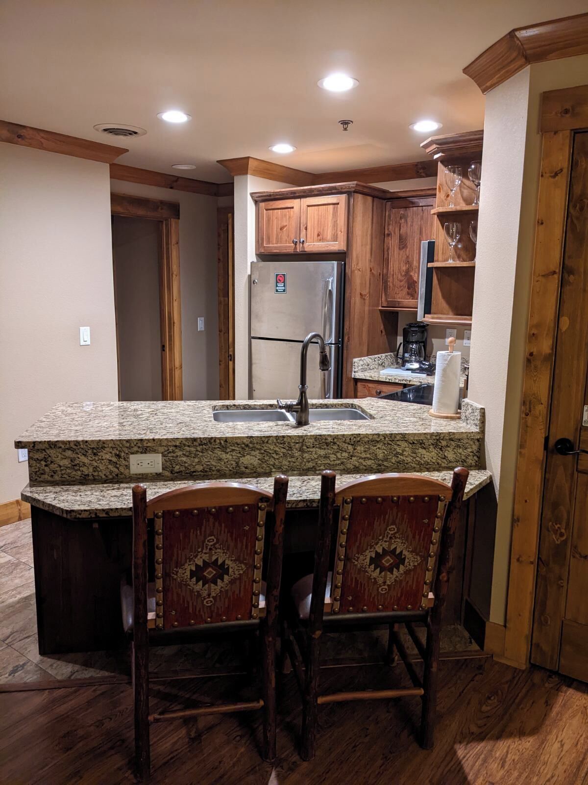 A kitchen with a granite countertop, stainless steel refrigerator, wooden cabinets, and a built-in sink.