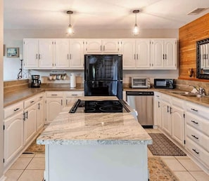 A kitchen with white cabinets, a central island, a black refrigerator, a microwave, and a stove.