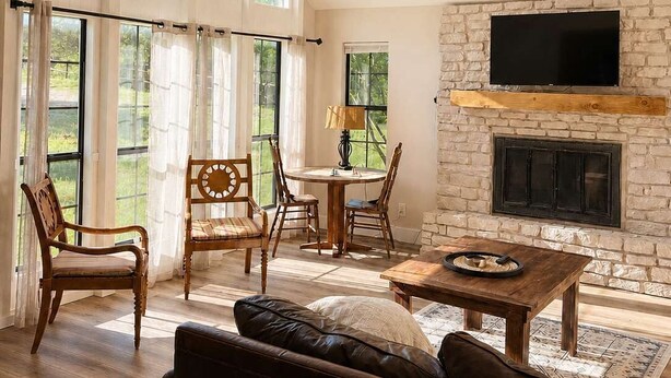 A spacious living room with a fireplace, large windows, and a ceiling fan. - Private Retreat w/ Animals. Outdoor Fire pit/ BBQ (Cedar Creek)