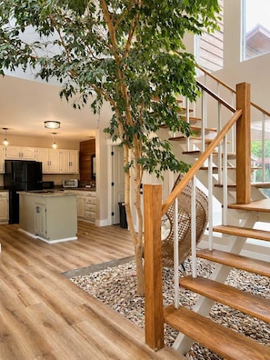 A spacious kitchen with wooden flooring, a central island, and a staircase with wooden railings.