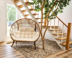 A wicker chair with cushions, a wooden staircase, and a tree in a room with a view.