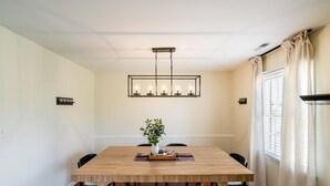 Un comedor con una mesa de madera, sillas, una lámpara de araña y una ventana con cortinas.