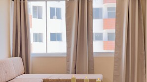 Una habitación moderna con sofá, una pequeña mesa con velas y vistas a un edificio a través de cortinas traslúcidas.