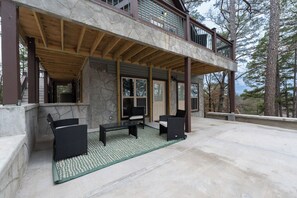 Un espace extérieur aménagé, abrité et doté de murs en pierre, de poutres en bois et offrant une vue sur les arbres.