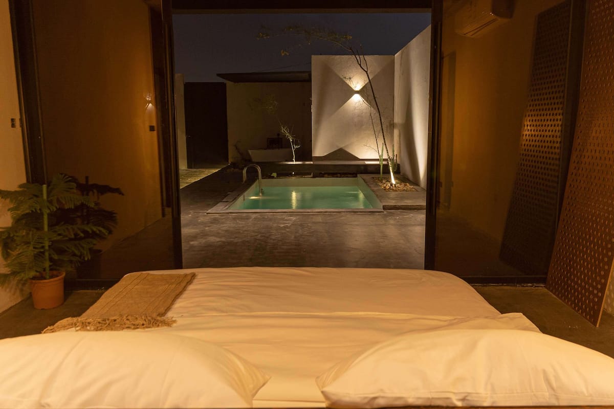 Un dormitorio con cama, vista a una piscina exterior y una planta en maceta.