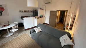 Ein kompakter Wohnbereich mit grauem Sofa, einem kleinen Esstisch und einer Küchenzeile.