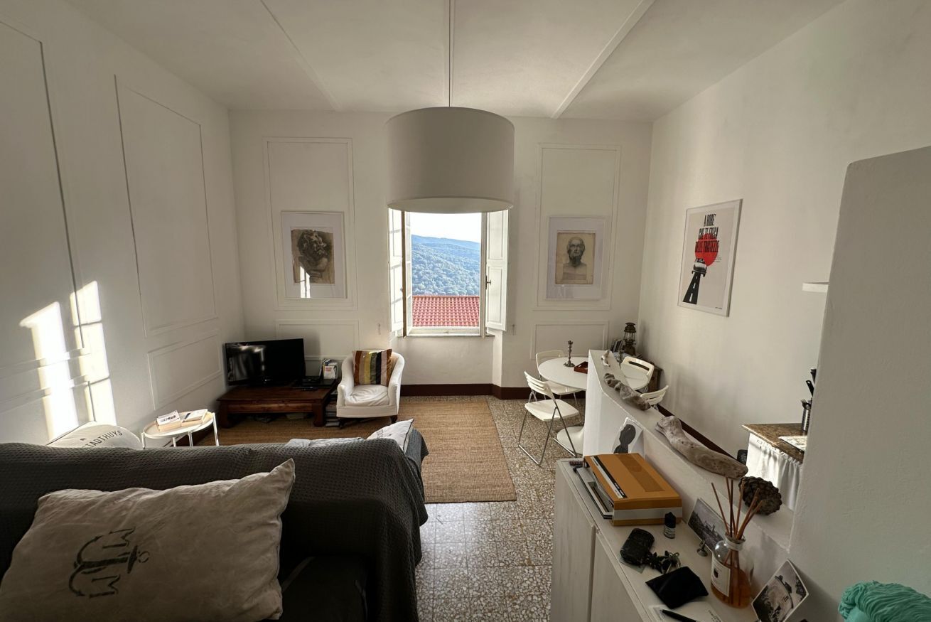 Quarto moderno e bem iluminado, com uma janela grande, televisão de tela plana, sofá, mesa pequena e escrivaninha com luminária.