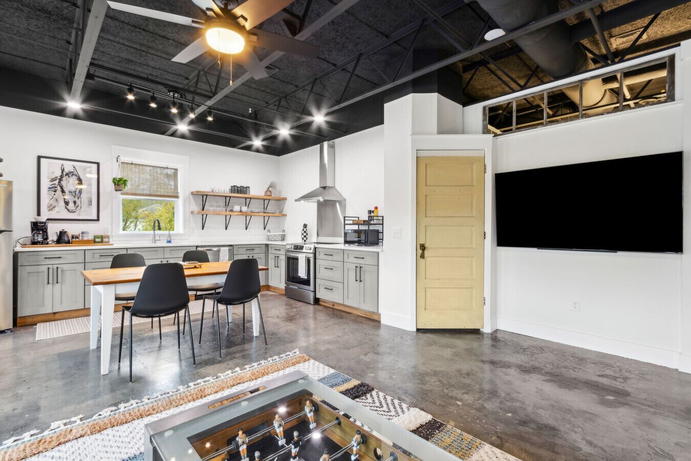 A modern kitchen with grey cabinets, a wooden dining table, and black chairs.