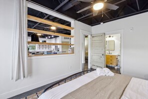 Une chambre à coucher avec un lit, une fenêtre avec des rideaux, un miroir et une porte donnant sur une salle de bain.