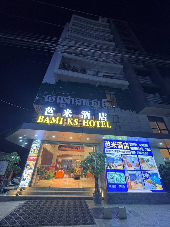 A hotel entrance with a neon sign in English and Chinese, a digital display with room images, and a QR code for reservations.